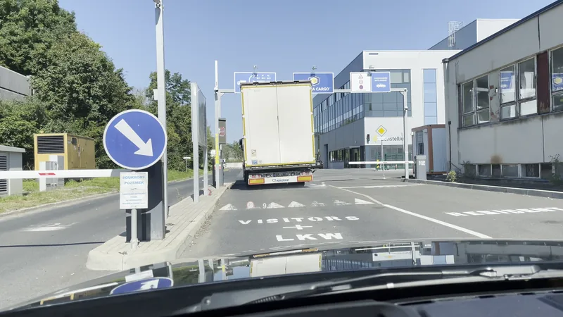 Pohled z kabiny: závora u vjezdu se zvedá, značka ukazuje směr k areálu